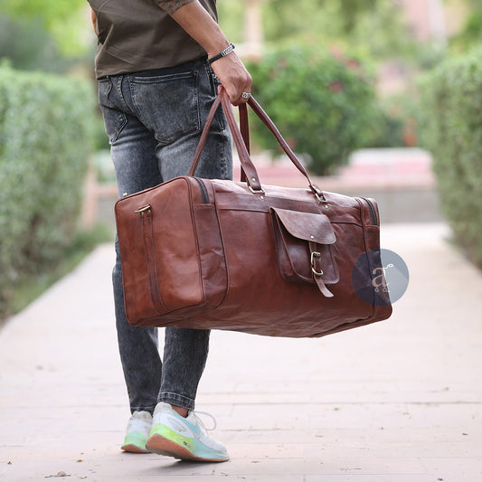 A Man Holding The Yachtsman Duffle By His Side, Wearing A Brown Shirt, Jeans, And Sneakers On A Pathway